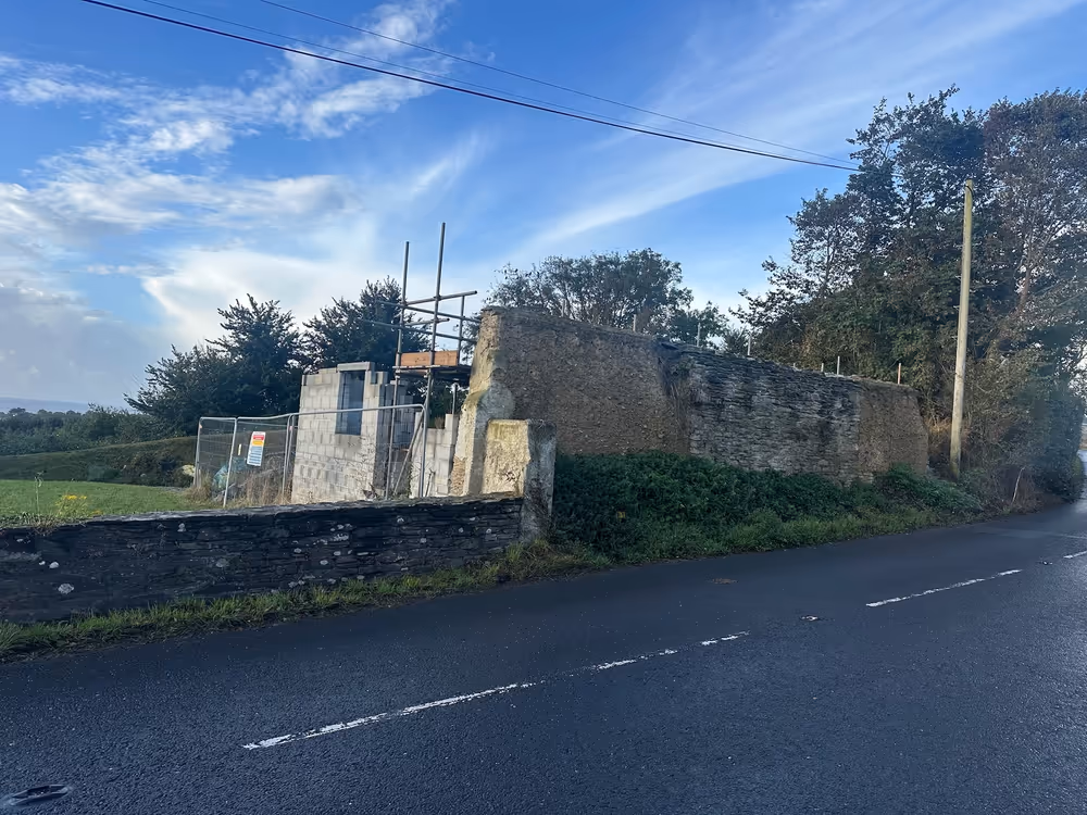 Original heritage farm building with the deteriorating roadside cob wall and early scaffold setup