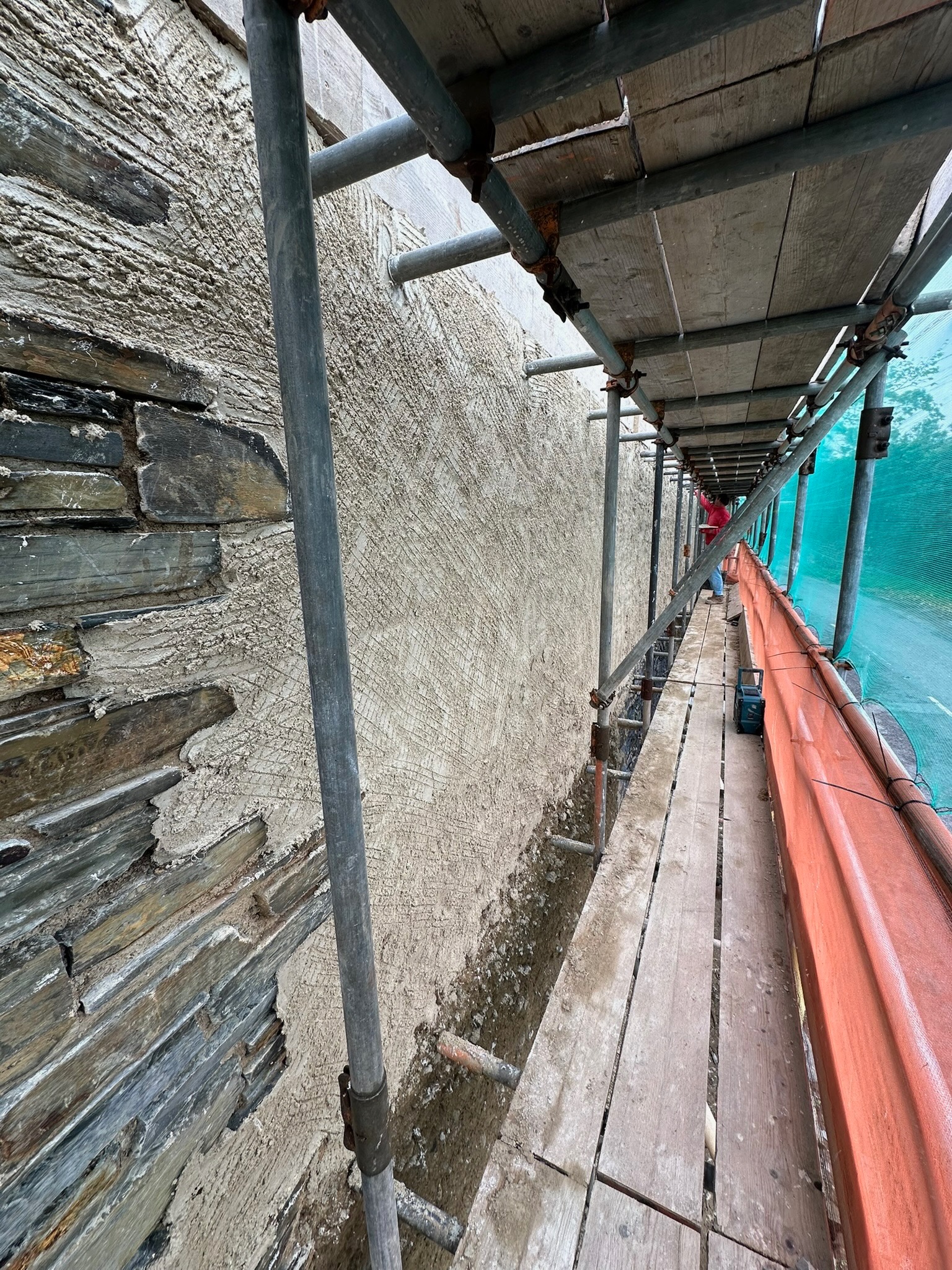 The first coat of natural lime render going on alongside the existing cob