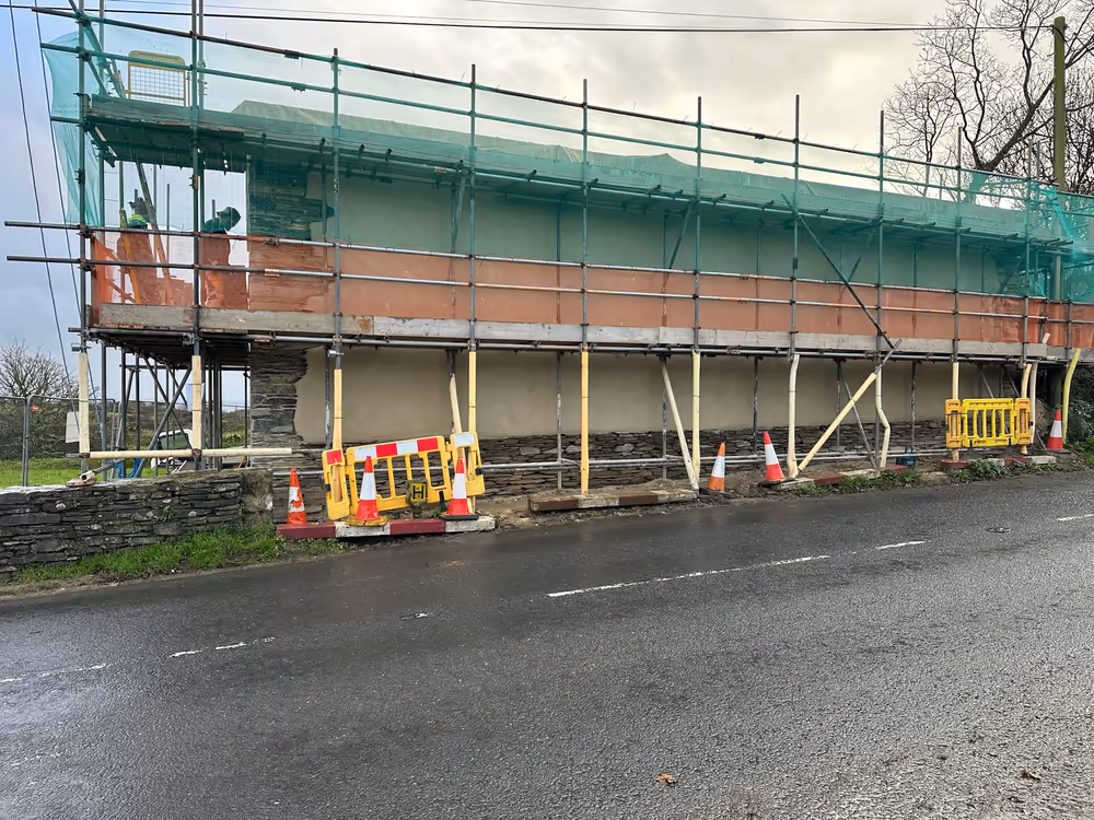 The rebuilt cob wall standing under scaffold during the works, seen from the road